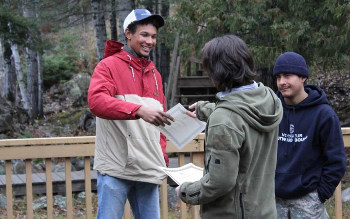 Three people speak and exchange papers during the family seminar of an outward bound intercept course.